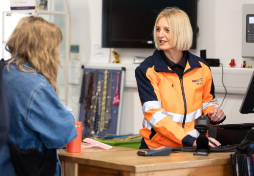 woman wearing hi-visibility clothing, serving a customer at the till in a shop