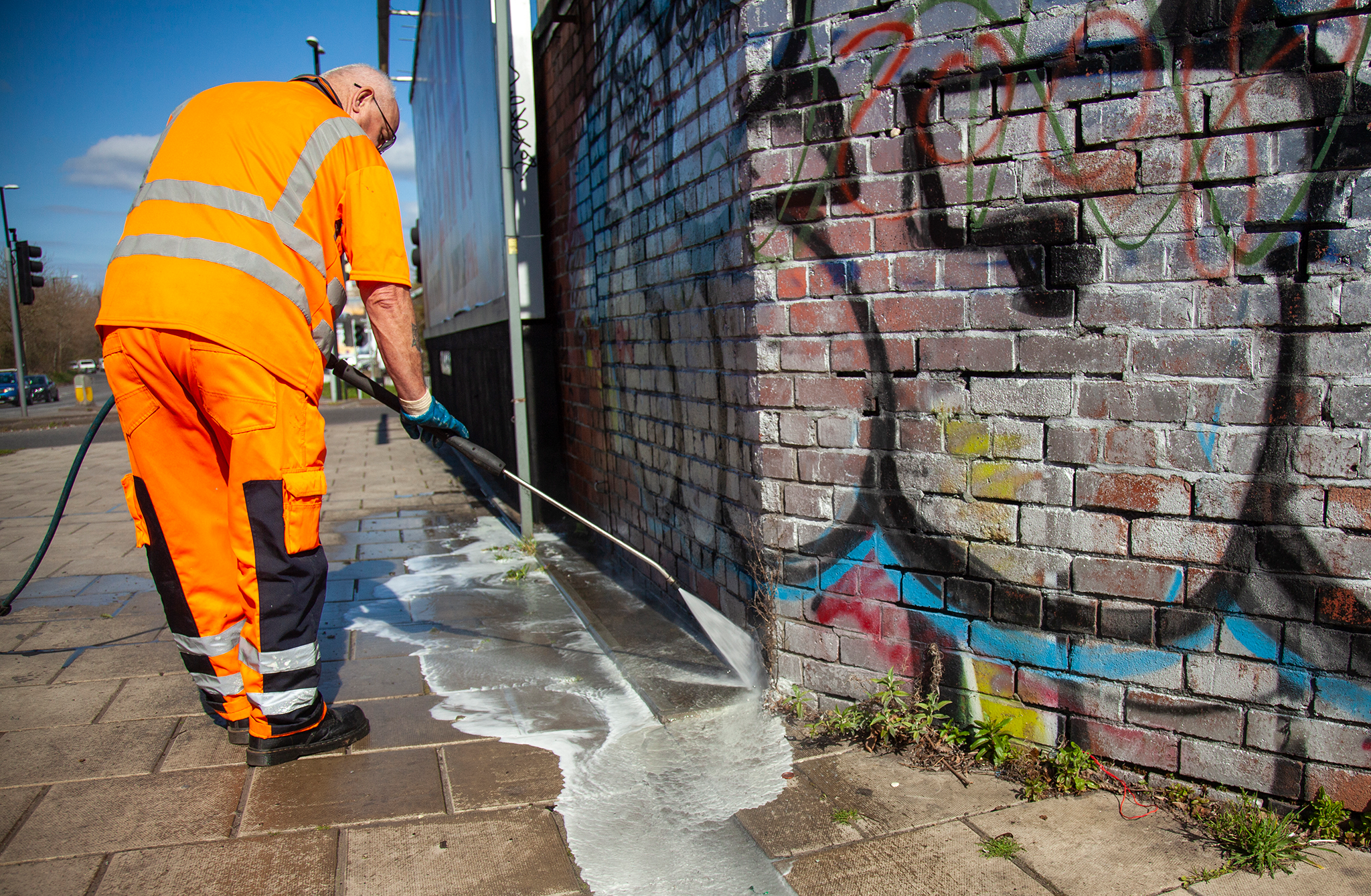 A Bristol Waste street cleansing operative using a jet washer to remove graffiti from a wall