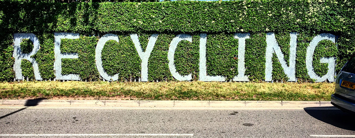 Large letters spelling out the word 'recycling' set into a roadside bush.