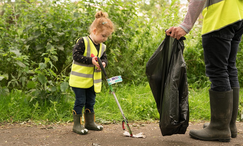 A small child uses a litter picker to collect a piece of plastic from the ground