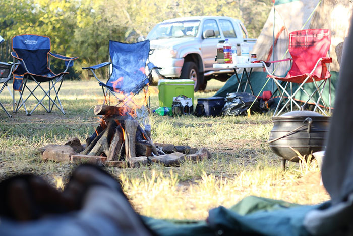 A campfire in a field with chairs surrounding it