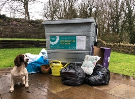 Large bin with a pile of rubbish and brown and white dog sitting next to it