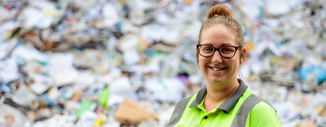 A smiling Bristol Waste employee stands in front of a pile of business recycling.