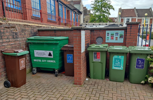 Large Bristol Waste recycling bins in front of a brick wall.