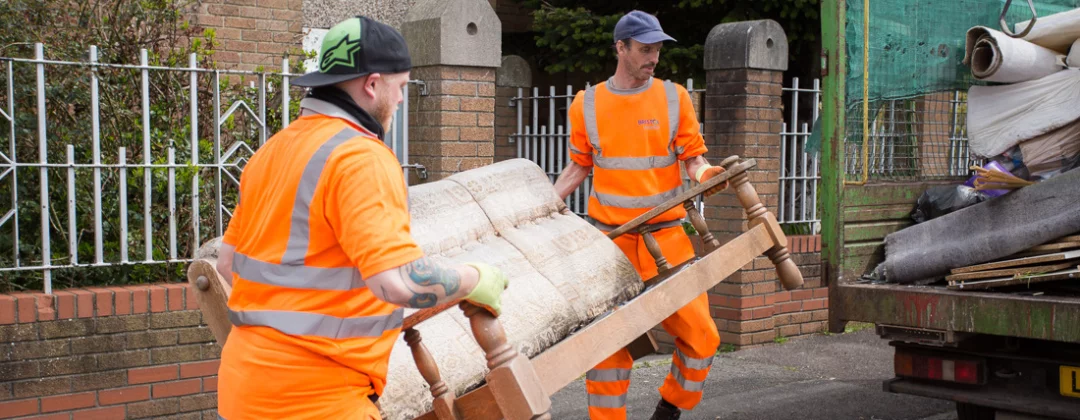 Two Bristol Waste crew members in orange hi-viz carrying a sofa
