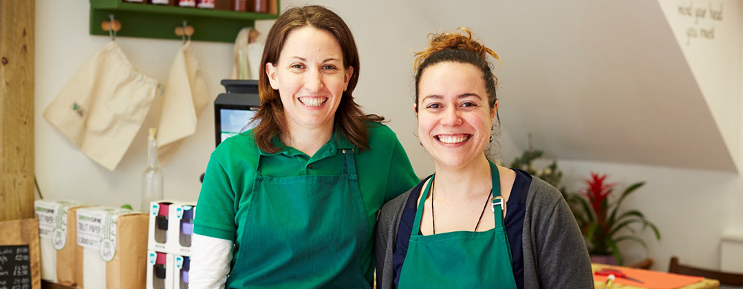 Two smiling women in green aprons