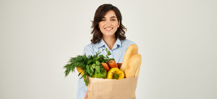 A smiling woman holding a brown paper bag full of food