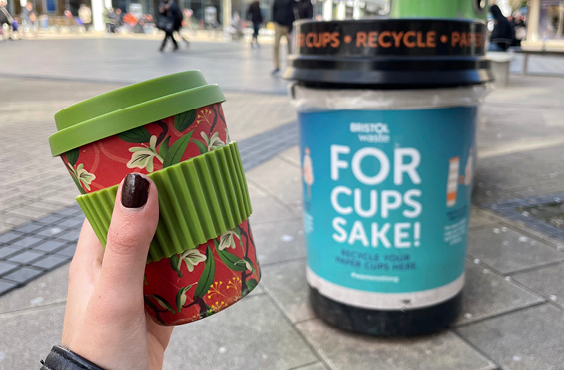 A reusable coffee cup being held in front of a cup bin