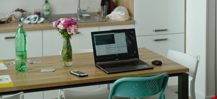 Image of a laptop on a kitchen table with a bunch of flowers and mobile phone next to it.