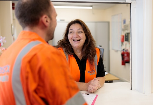 Two Bristol Waste employees smiling whilst standing at a desk wearing high vis uniforms