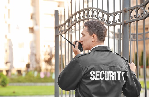 Male security guard with a walkie talkie standing next to a gate