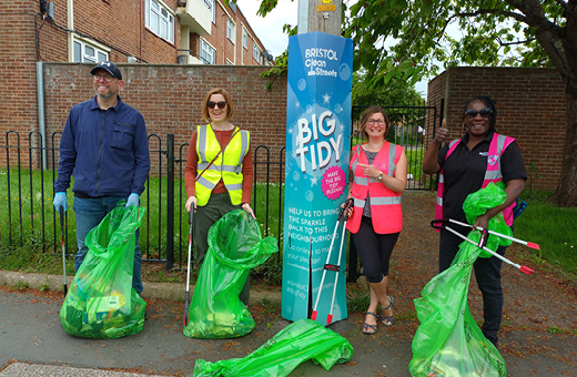 Four people litter picking standing next to a big tidy sign