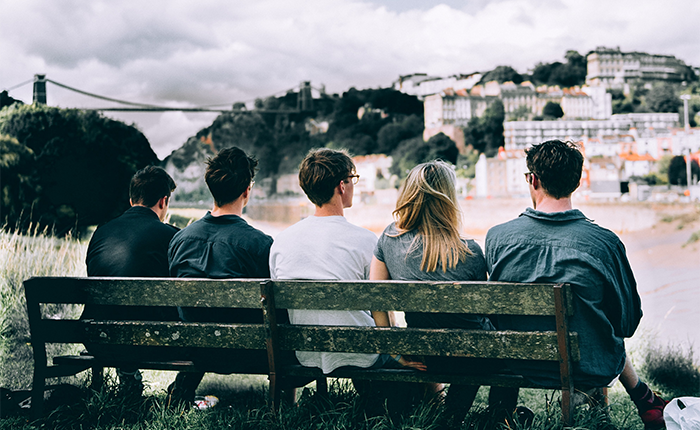 a photography of five students sitting on a bench with their backs to the camera. In the distance is clifton and the suspension bridge.