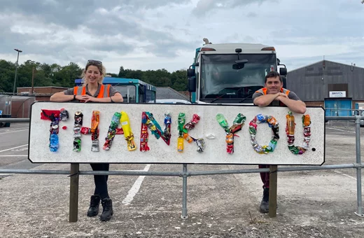 Two Bristol waste staff leaning on a sign made from rubbish. The sign says thank you