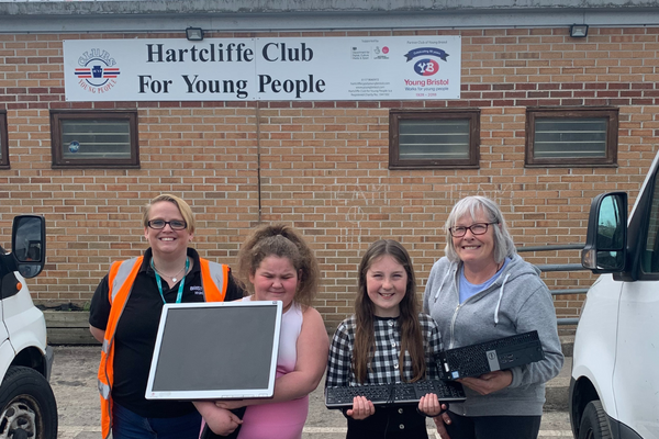 Two women and two children holding a laptop and keyboard in front of a youth club.