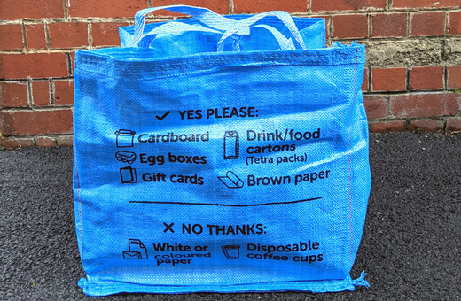 A Bristol Waste blue bag for card and brown paper in front of a red brick wall.