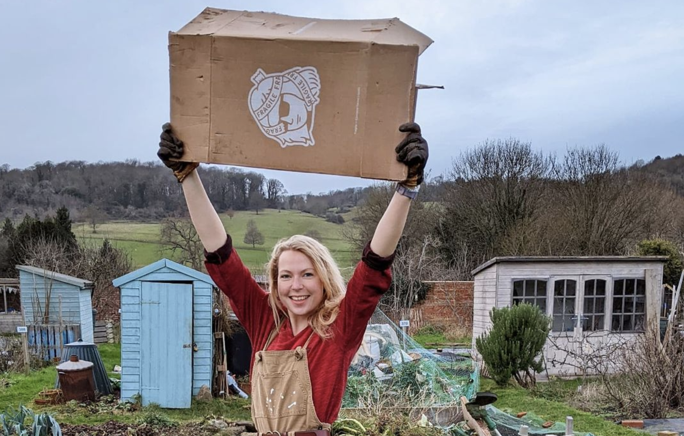 Jenny on her allotment holding a sheet of cardboard above her head