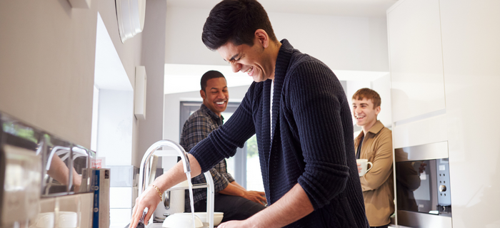 Three male students laughing together in a shared kitchen while one does the washing up