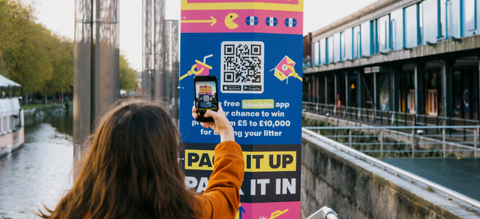 A woman scans a Bristol's binning QR code on her phone to sign up to the LitterLotto app