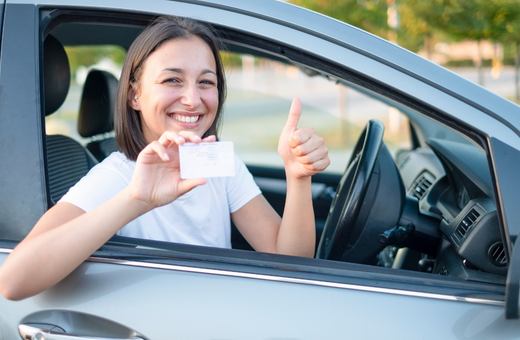 A smiling woman shows her ID through her car window whilst giving a thumbs up with her other hand