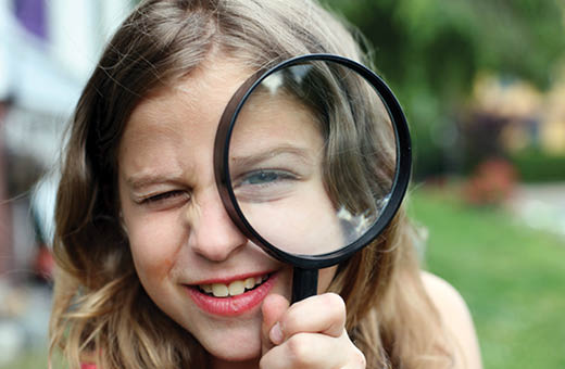 A young girl looking through a large magnifying glass