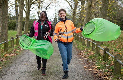 Naomi and Hannah walking down a park path with litter bags