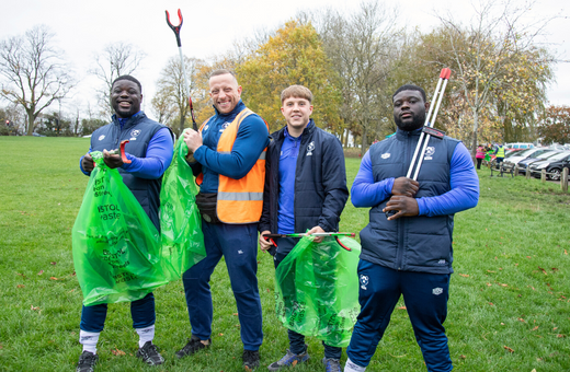 Four men in a park smiling at the camera and holding litter pickers and litter bags