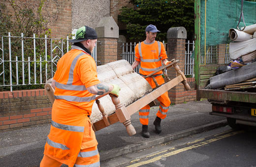 Two refuse collectors picking up an old sofa left on the street to put in the back of a van