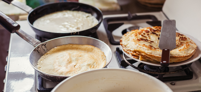 Two frying pans with pancakes inside on stove top, a plate of cooked pancakes to the side.
