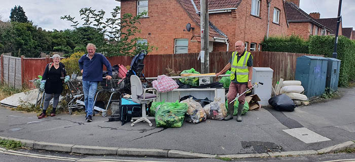 Three people standing next to a lot of rubbish that has been gathered from fly-tips
