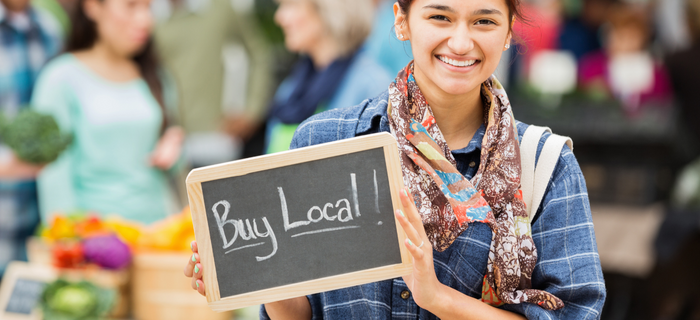 A smiling woman holds a chalkboard sign that reads 'shop local'.