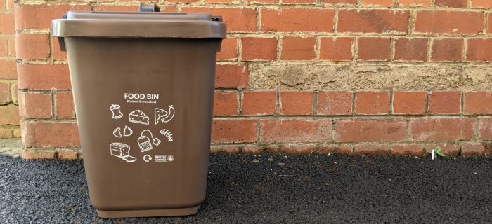A Bristol Waste food bin on the pavement next to a red brick wall