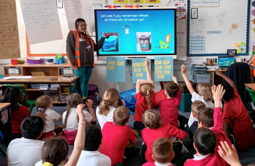 A class of primary school children sit cross legged on the floor of their classroom, watching a presentation from a Bristol Waste community engagement officer.