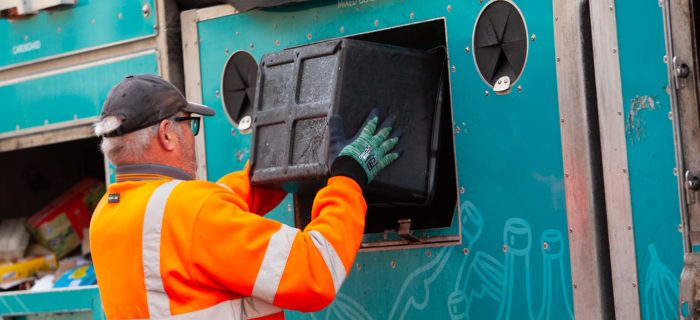 A Bristol Waste recycling crew member empties a black recycling box into the collection vehicle