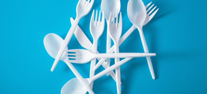 A small bundle of white single use plastic cutlery on a blue background.