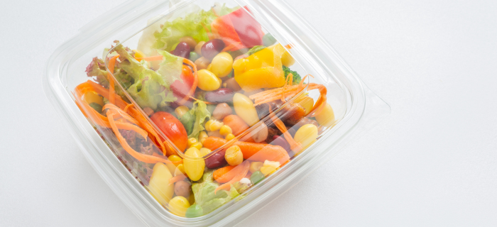A salad in a clear single-use plastic box on a white background.