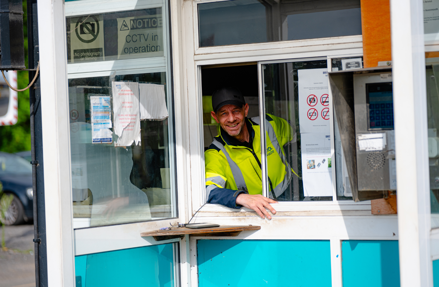 A smiling person leans out of the window in a porta cabin at the Bristol Waste site