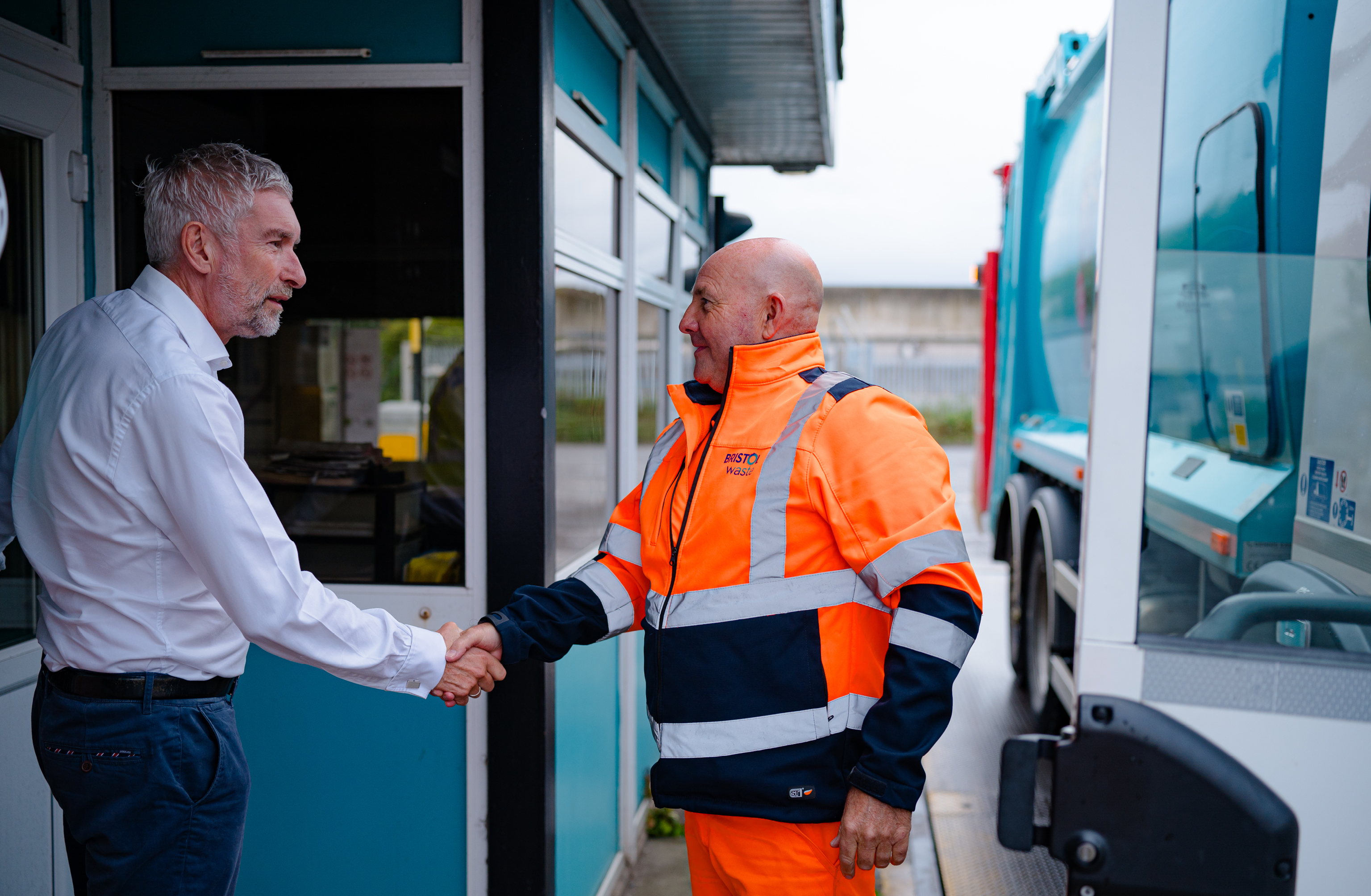 Two men shake hands one is wearing a shirt the other hi-viz PPE