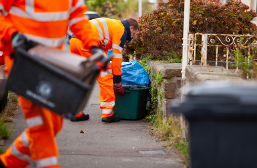 A collection crew picking up a green recycling bin from a Bristol street.