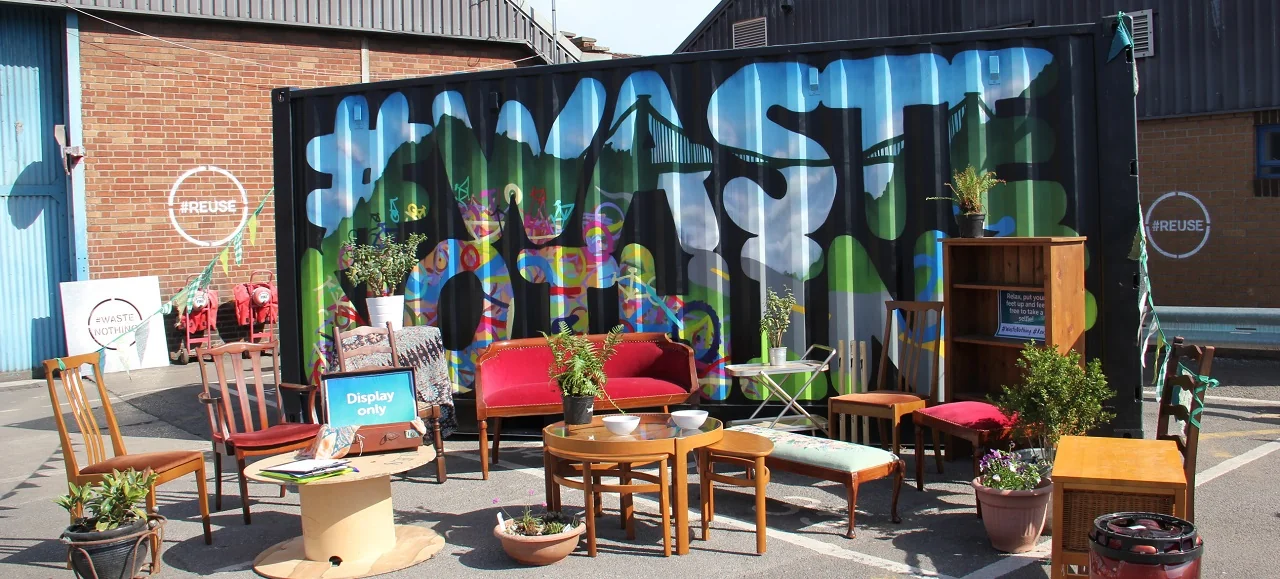 A selection of second hand furniture is arrange next to a painted sign that says #WasteNothing