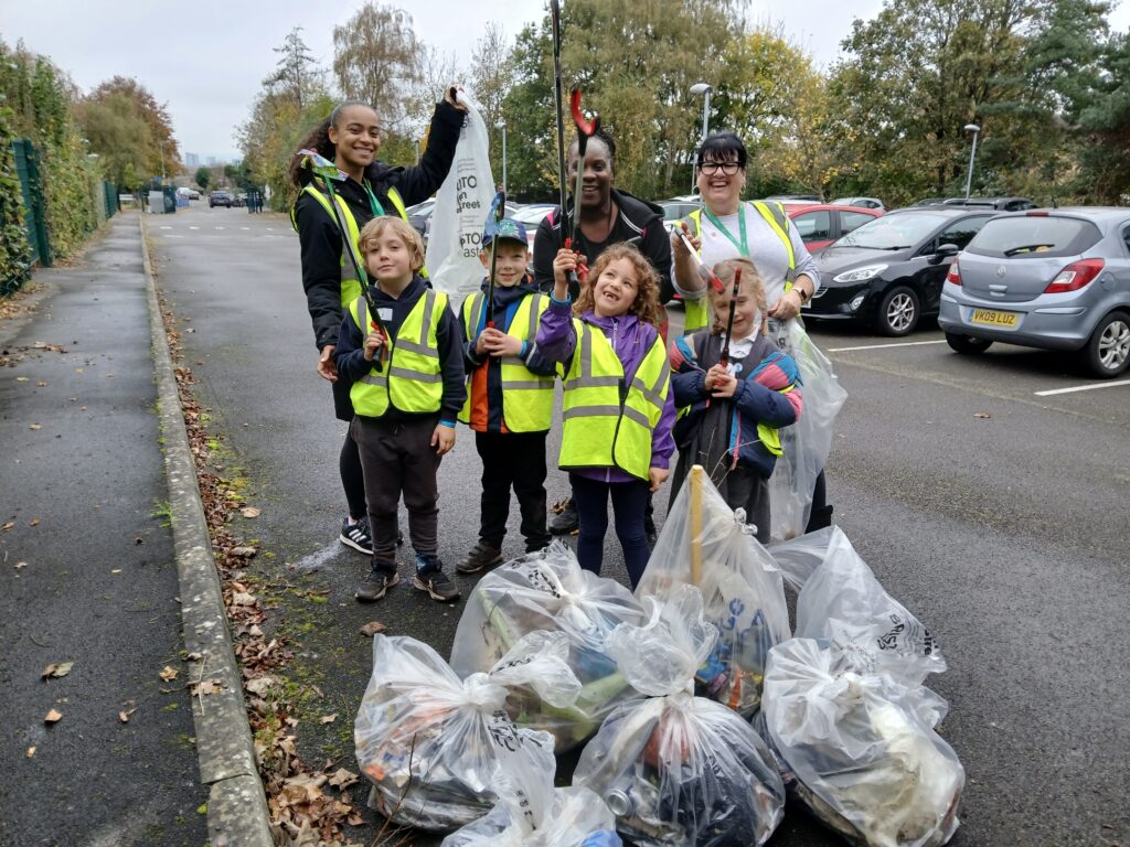 A group of children and adults holding litter pickers, they are standing behind a pile of filled litter bags.