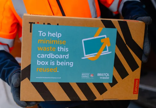 Person carrying back that reads "to help minimise waste this cardboard box is being reused."