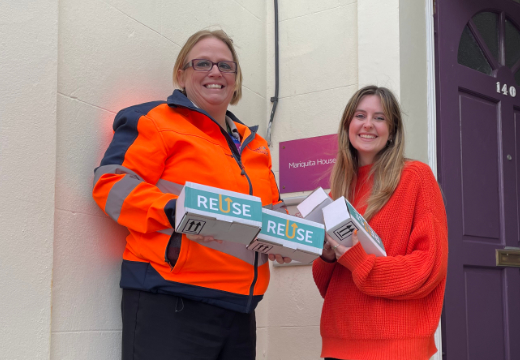 Two women smiling, holding boxes that say "reuse"