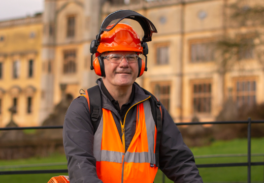 Man in high visibility clothing, wearing a hard hat and visor in front of a big building.
