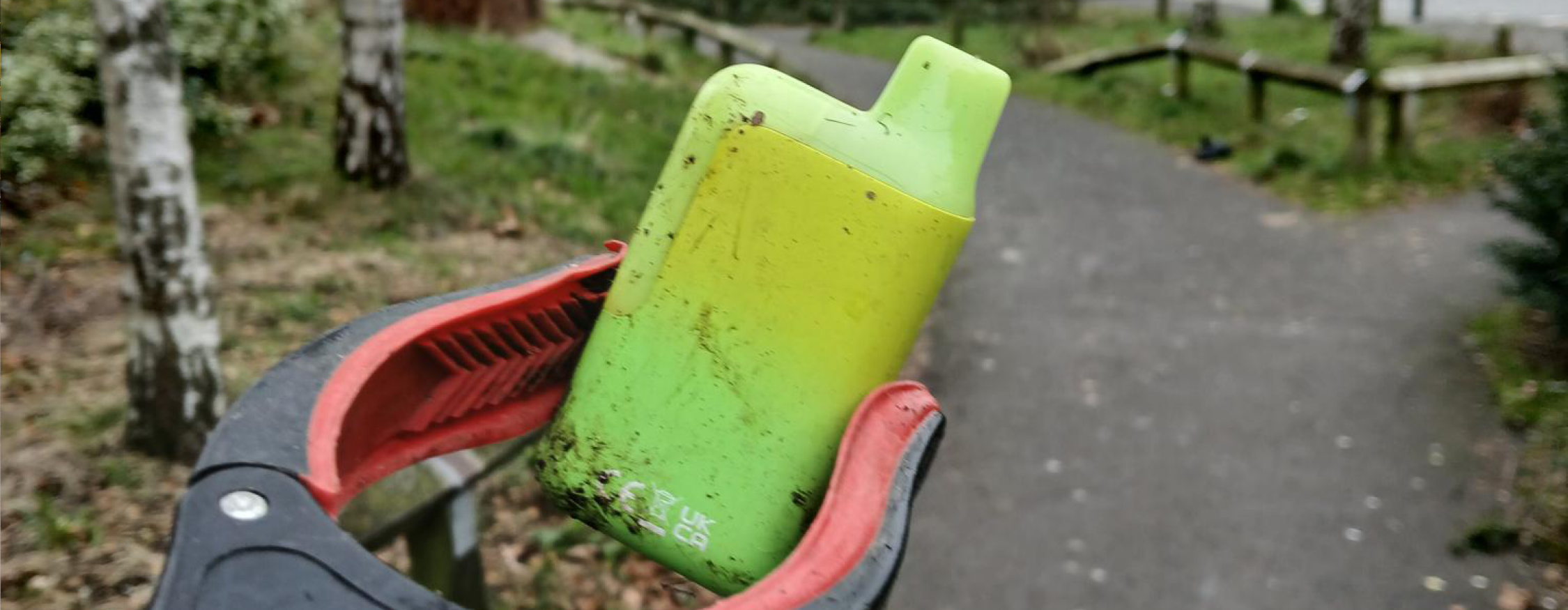 A litter picking stick holds up a brightly coloured disposable vape