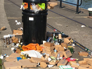 A bin on Bristol's harbourside is overflowing with rubbish. A mountain of old card and litter is on the floor next to it