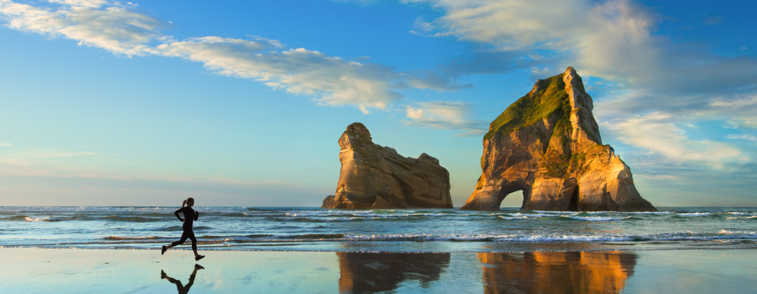Windows 10 default wallpaper, person running across a beach with small islands on the beach