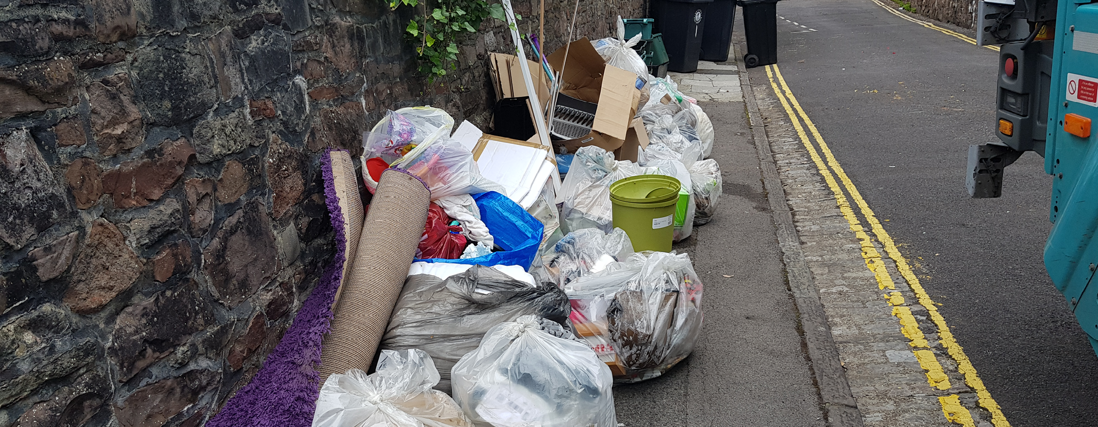 A pile of illegally dumped rubbish on a pavement. There are bags, rolled up carpet and other horrible fly-tipped items in the pile