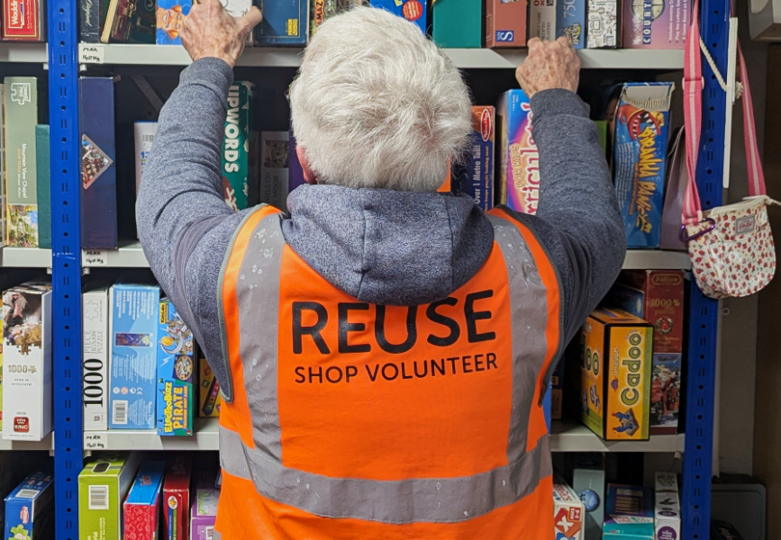 Person organising shelfs of board games wearing a reuse shop volunteer vest