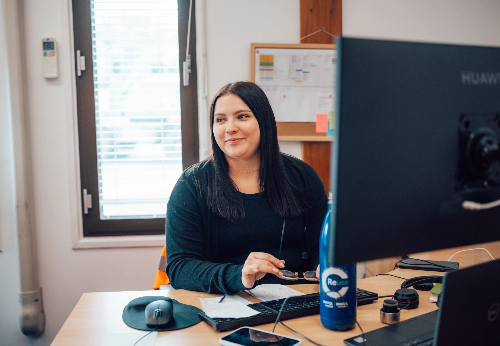 Woman sat at desk in front of computer screen, smiling
